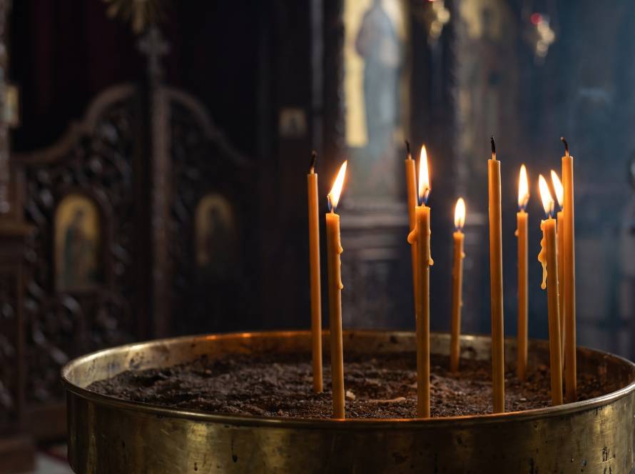 Thin beeswax candles burning in a brass sand tray inside a dim Orthodox church.